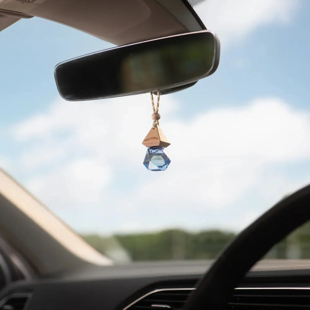 Car interior with a blue crystal hanging from the rearview mirror against a blurred outdoor background.